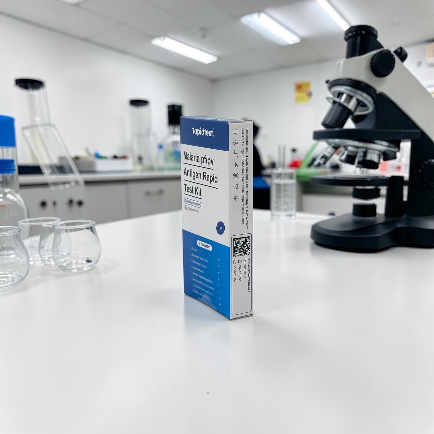 Malaria test kit box on a laboratory counter with a microscope in the background